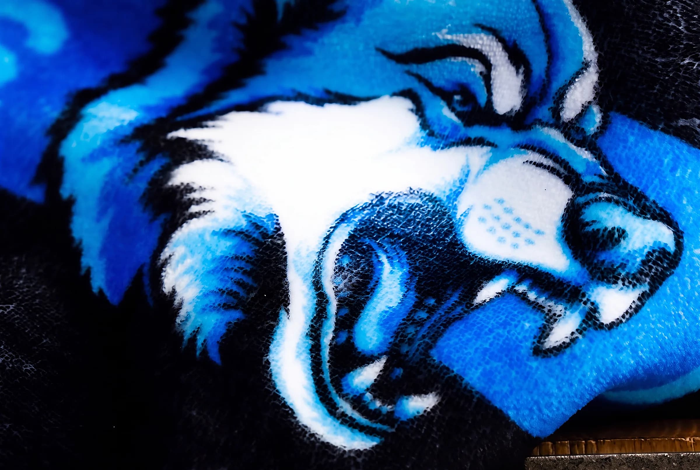 Extreme macro of a blue wildcat mascot sublimated into plush blanket pile, ink resolved in individual fibers